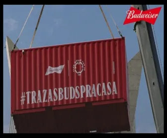 Contêiner vermelho da Budweiser com a hashtag #TRAZASBUDSPRACASA sendo içado em ação promocional.